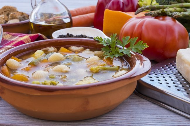 A fresh, ready-to-eat homemade vegetable soup. Raw vegetables on the wooden table, black pepper, olive oil and parmesan